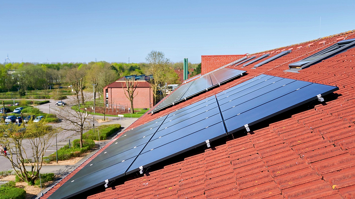 Auf dem Dach eines Hauses ist eine Photovoltaikanlage montiert, die aus mehreren aneinandergereihten Solarplatten besteht.
