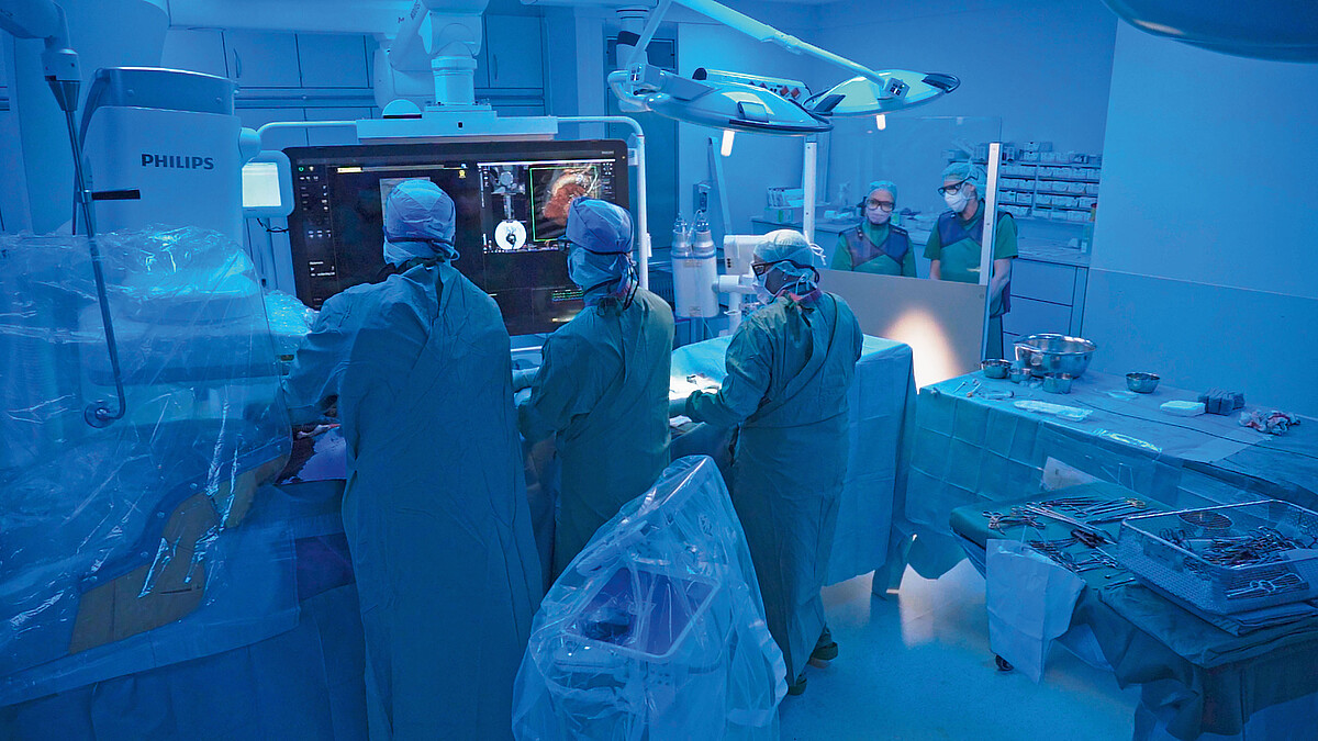 Medizinisches Personal schaut in einem OP-Saal auf einen großen Monitor.