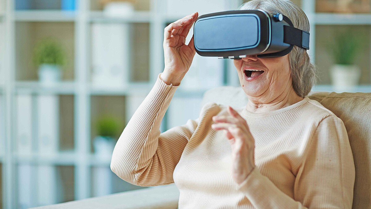 Eine Seniorin trägt eine VR-Brille und lacht überrascht.