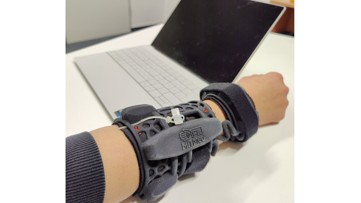 Das Bild zeigt einen Arm mit einer Manschette mit Sensoren. Daneben steht ein Laptop.