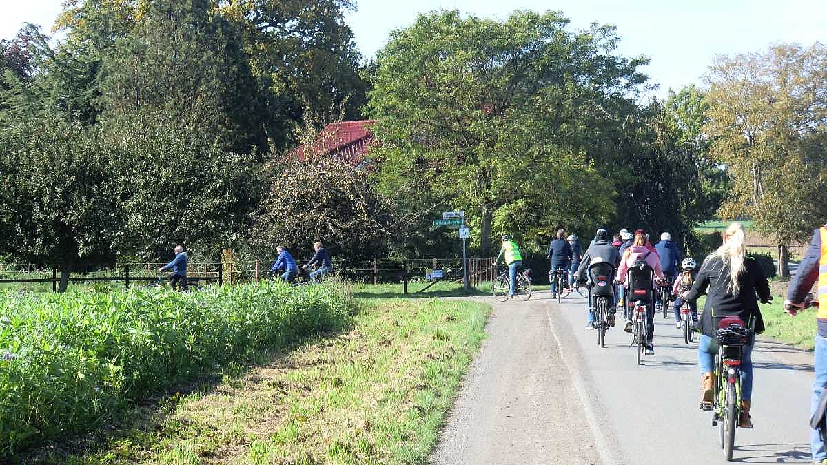 Eine Gruppe fährt mit dem Fahrrad an Feldern und Gärten vorbei.