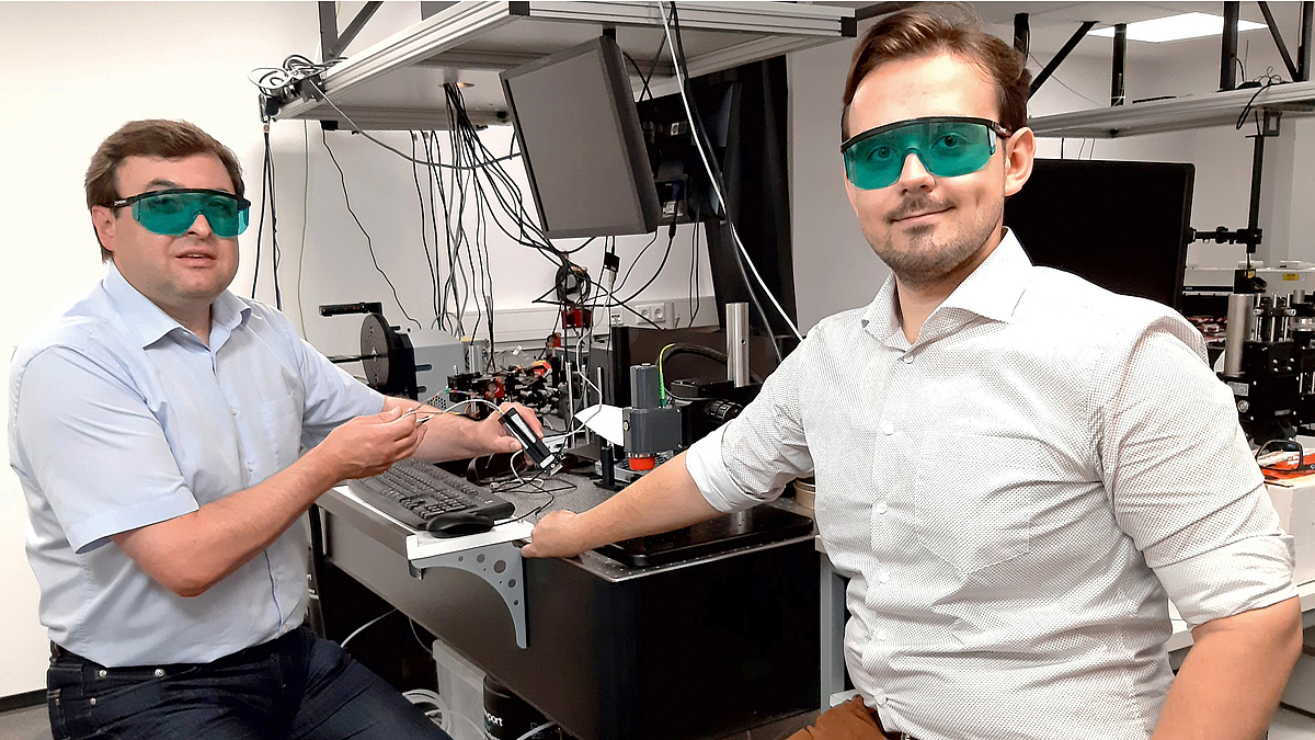 Zwei Wissenschaftler mit Schutzbrillen sitzen in einem Labor mit einem Lasergerät zur Hautkrebsdetektion