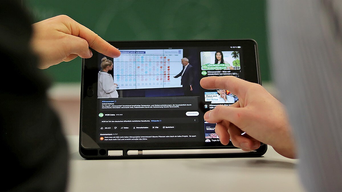 Zwei Hände zeigen auf ein Tablet, auf dem ein YouTube-Video zu sehen ist. 