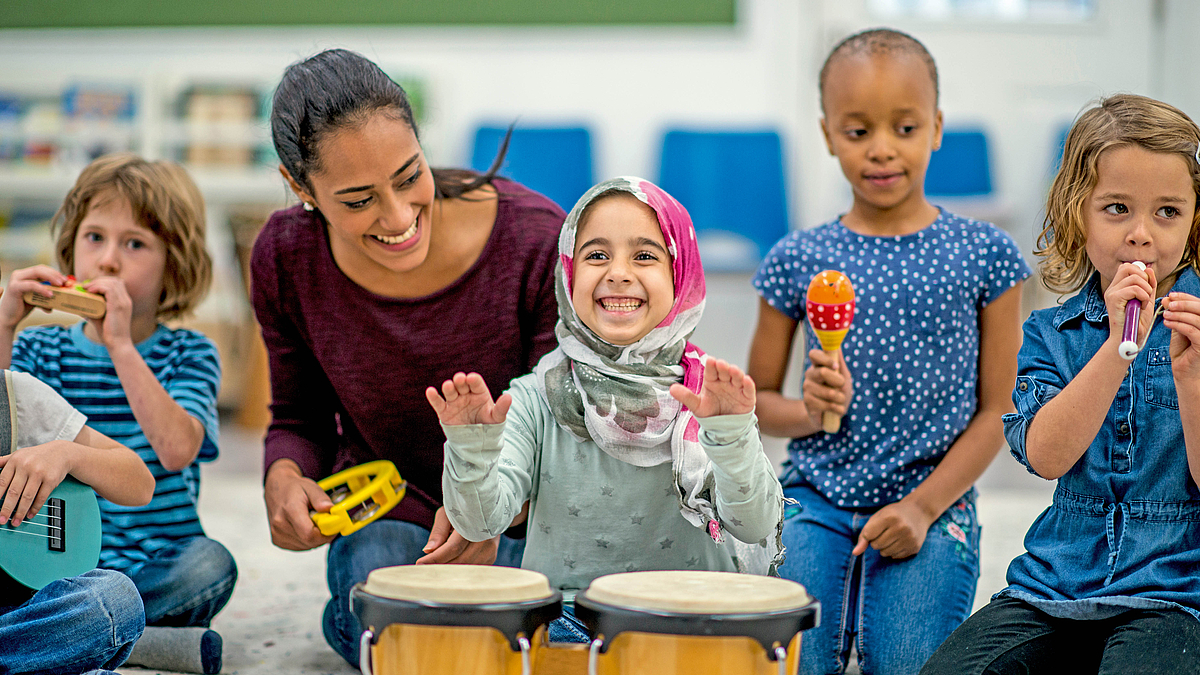 Lächelnde Kinder musizieren mit einer Betreuerin.