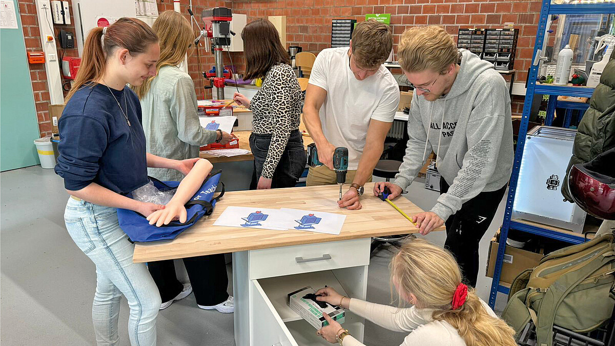 Junge Menschen arbeiten in einer Werkstatt mit einer Arm-Attrappe und Werkzeugen.