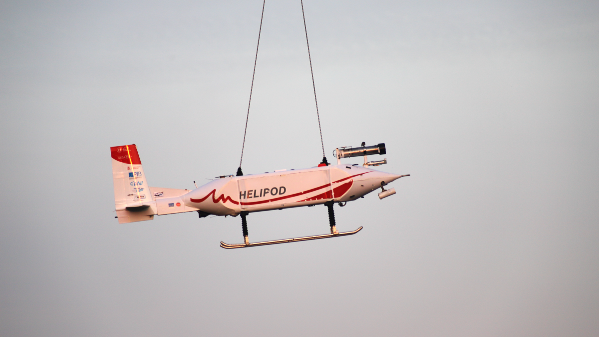 Die stromlinienförmige Sonde mit Messgeräten, Steuerruder und Kufen hängt an einem Seil unter dem Hubschrauber.