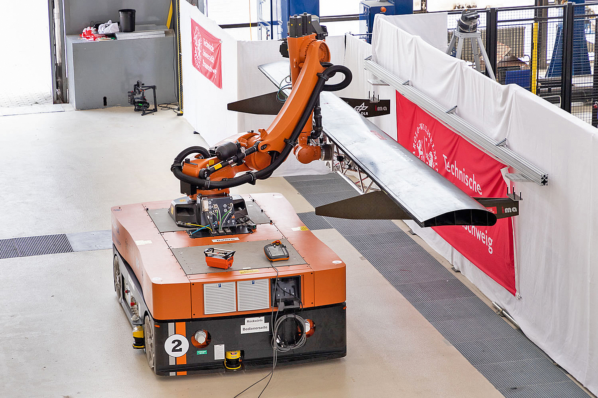Der Roboterarm hebt das Bauteil an eine Montageschiene.
