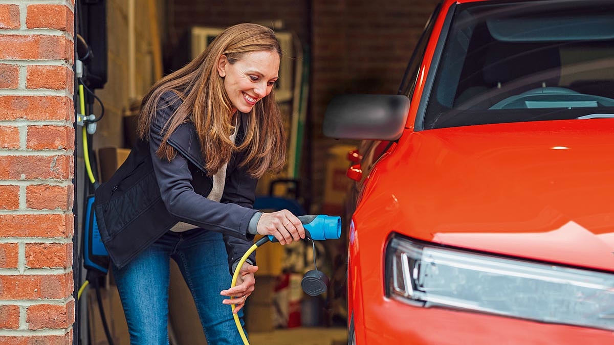 Eine Frau steckt das Ladekabel in ihr Elektroauto in der Garage