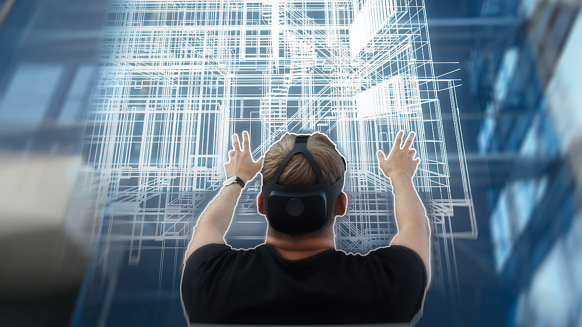 Ein Mann mit einer Virtual-Reality-Brille steht vor einer virtuellen Projektion eines Gebäudes.