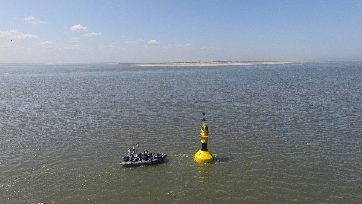 Ein Messboot hält in der Nähe einer Gefahrentonne. Am Horizont zeichnet sich die Insel Spiekeroog ab.