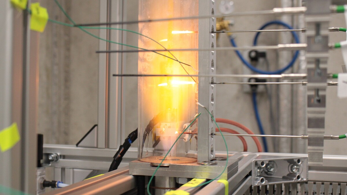 In einen Glaskolben strömt Gas ein, dass sich entzündet. Zwei drahtförmige Thermoelemente glühen.