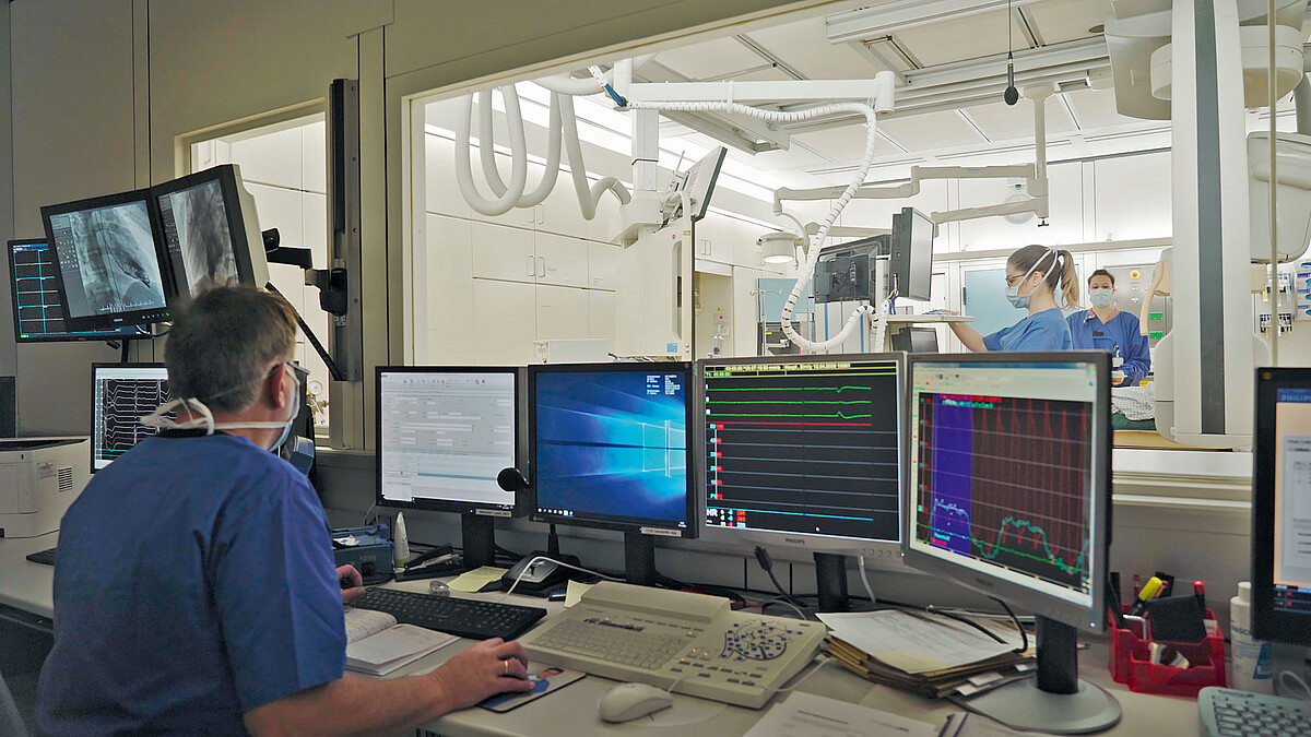 In einem Kontrollraum neben einem OP-Saal schaut ein Mitarbeiter auf viele Monitore.
