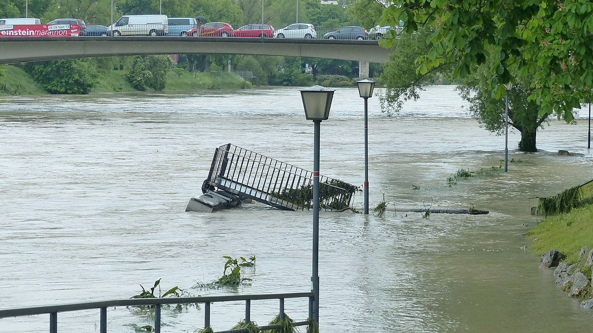 Ein Fluss ist über die Ufer getreten und hat einen Steg weggerissen. Über eine Brücke fahren viele Autos.