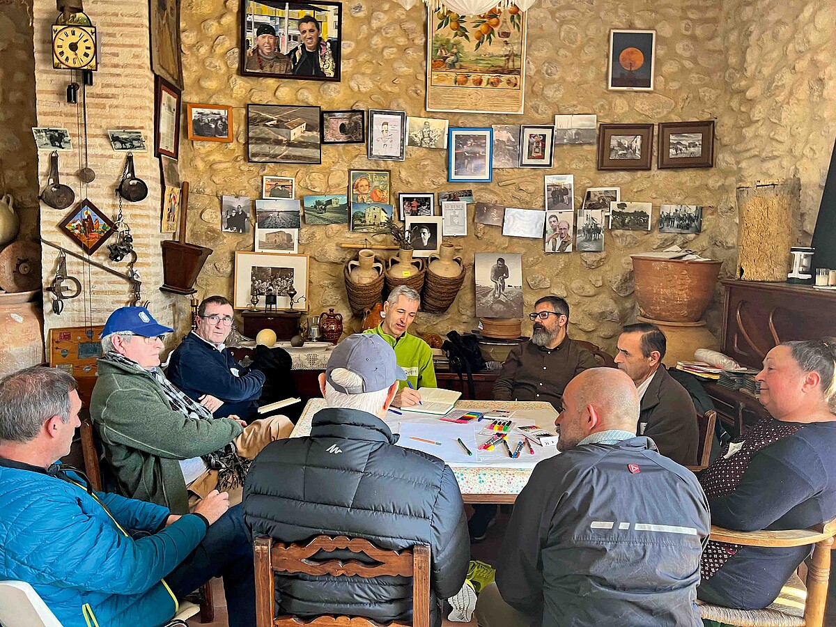 Menschen sitzen in einem üppig dekorierten Café um einen Tisch mit Arbeitsmaterialien.