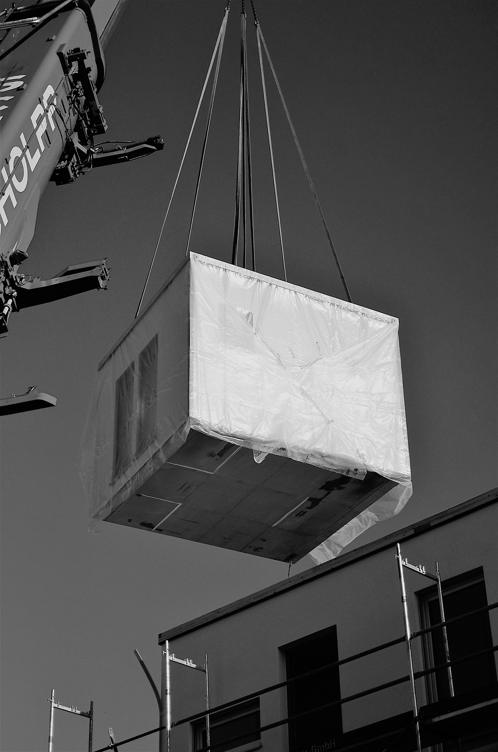 Ein containerförmiges Raummodul wird von einem Kran mit Hilfe von Seilen getragen