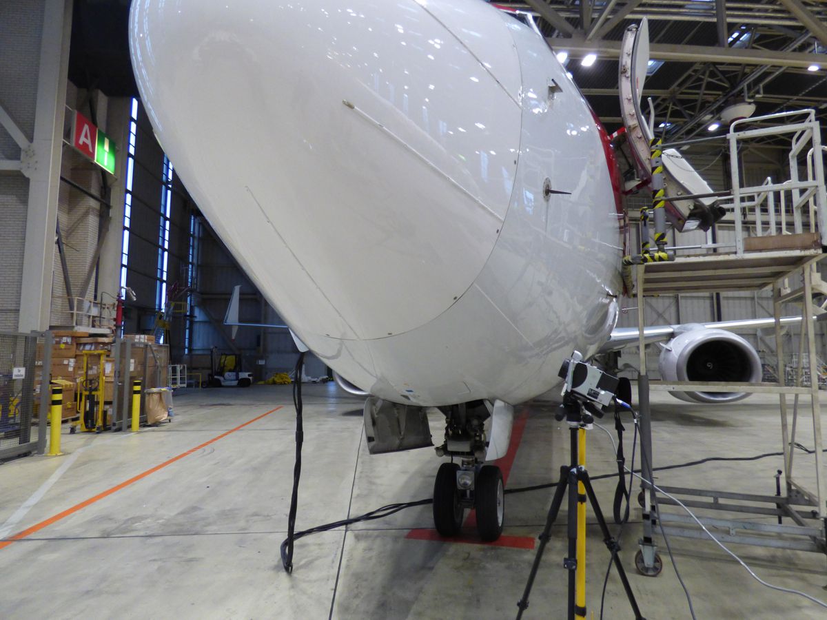 Vorderansicht eines Flugzeuges, das sich in einem Hangar befindet. Davor steht eine Thermografiekamera.