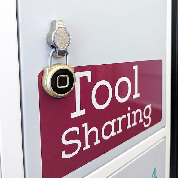 An einem Schrank mit Schriftzug Tool Sharing hängt ein elektronisches Vorhängeschloss.