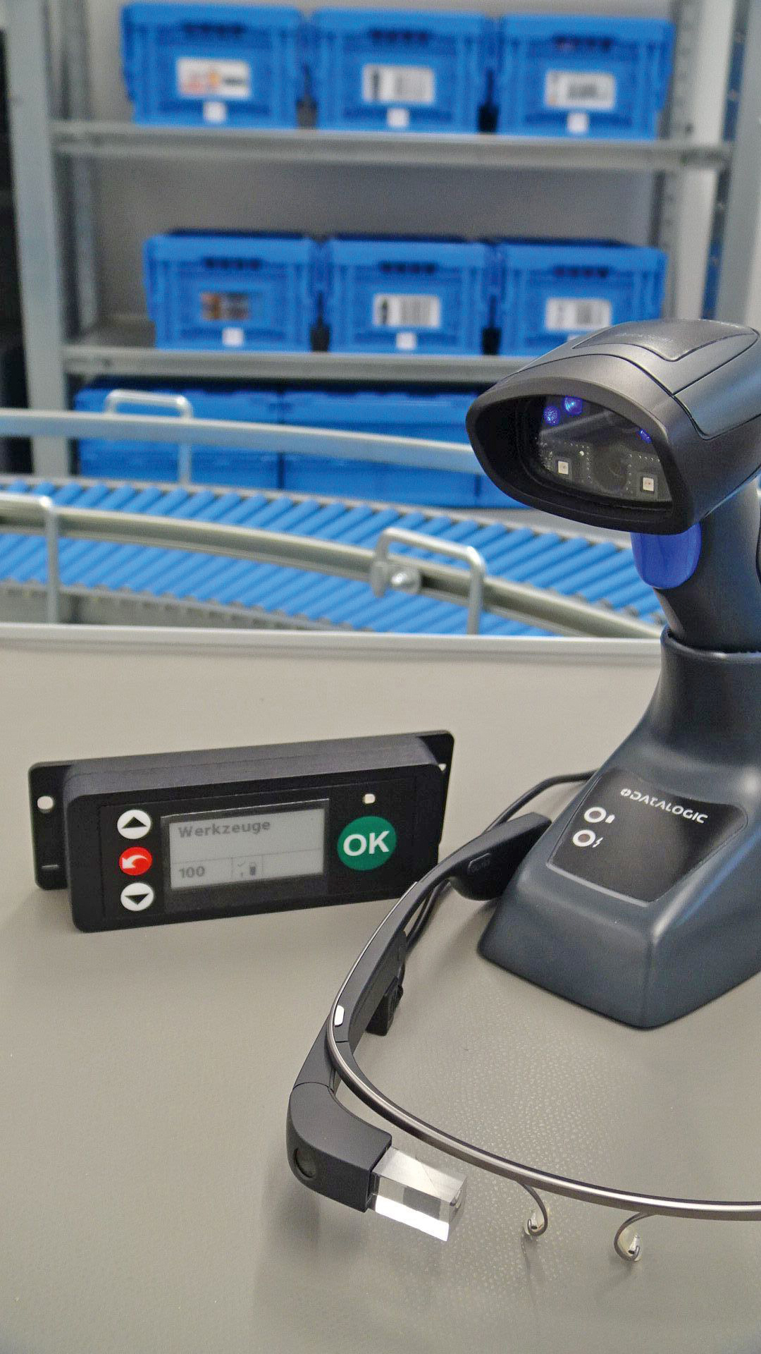 Ein Handscanner und eine Steuerungsbox stehen vor einem Warenlager.