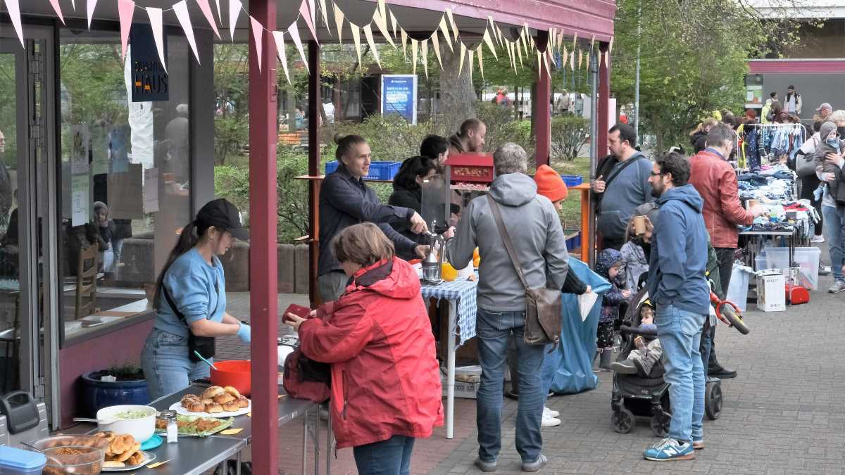 Menschen treffen sich an Ständen mit Speisen- und Kleidungsangeboten.