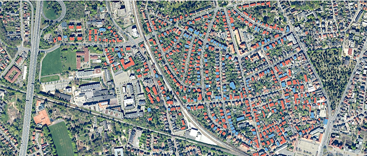 Ein Luftbild zeigt Wohn-, Wirtschafts- und Grünflächen, Straßen sowie verschieden markierte kleine und große Gebäude.