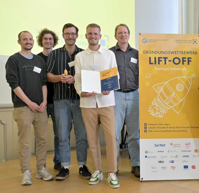 Fünf Männer stehen neben einem Banner des Gründungswettbewerbs LIFT-OFF. Lächelnd zeigen sie eine Urkunde in die Kamera.