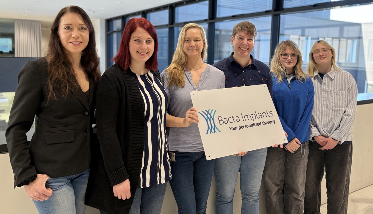 Auf dem Gruppenfoto mit 6 Frauen halten die beiden in der Mitte das Projekt-Logo „Bacta Implants – your personalized therapy“ in der Hand.